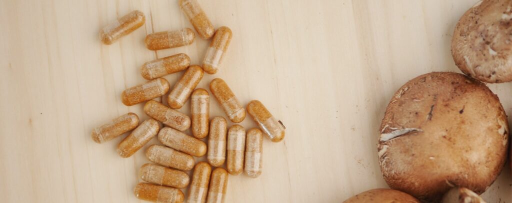Mushroom supplement capsules and raw mushrooms on a wooden surface.