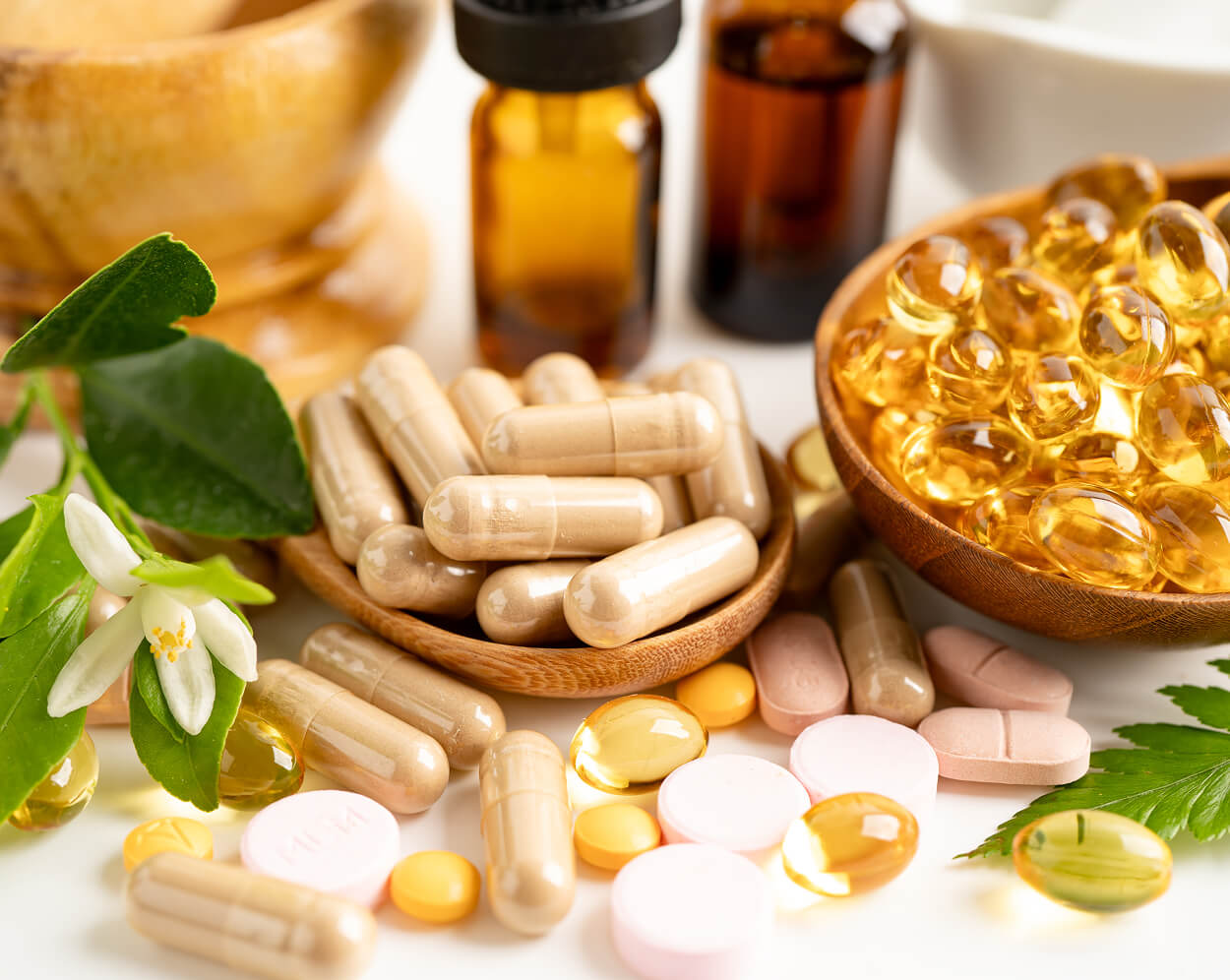 Various medicines and vitamins in wooden bowls on a white surface.