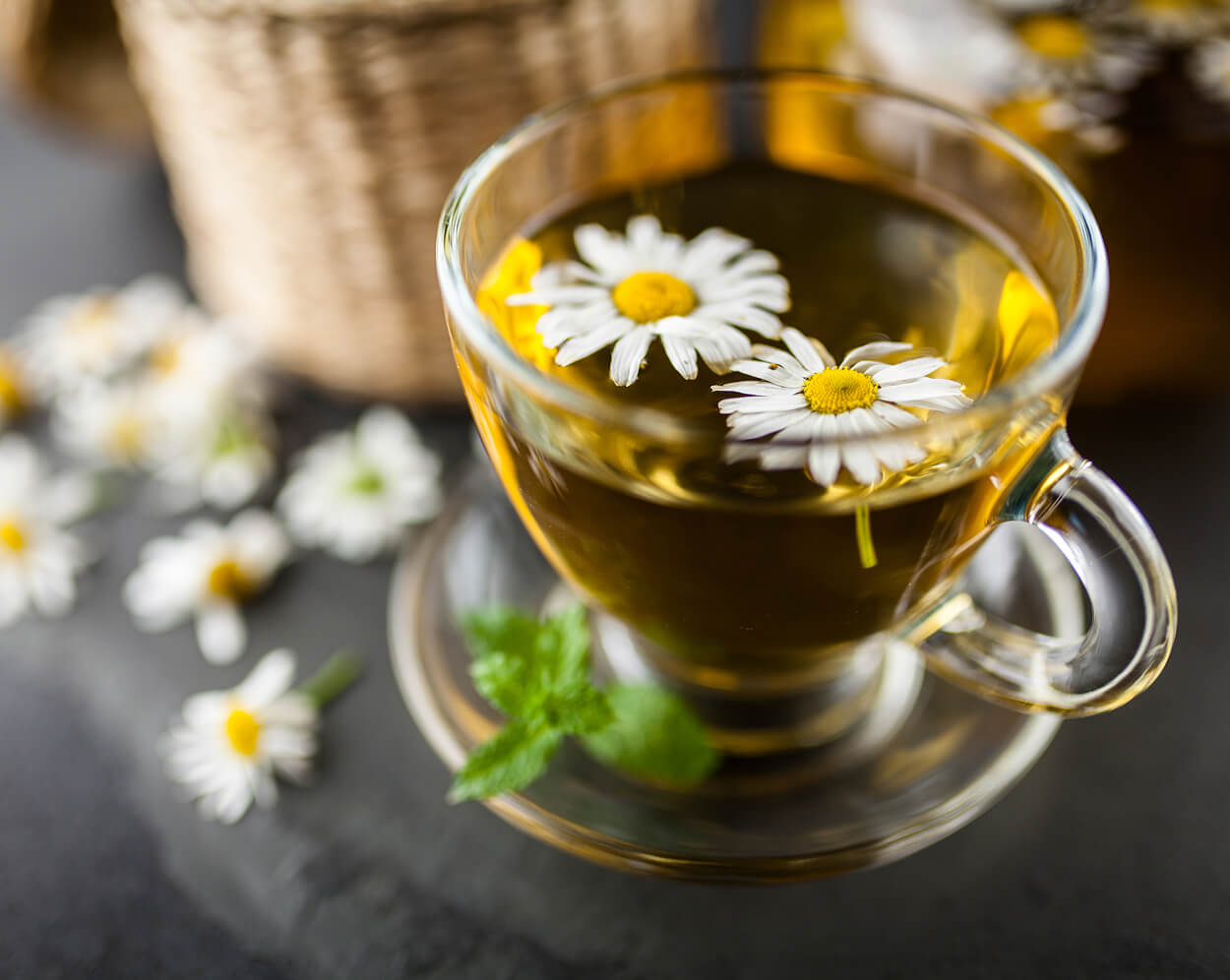 Chamomile tea in a glass cup with blurred background.
