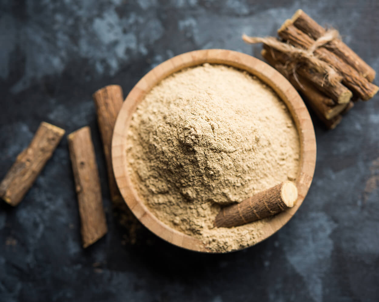Liquorice root stick and powder served in a bowl over moody background.