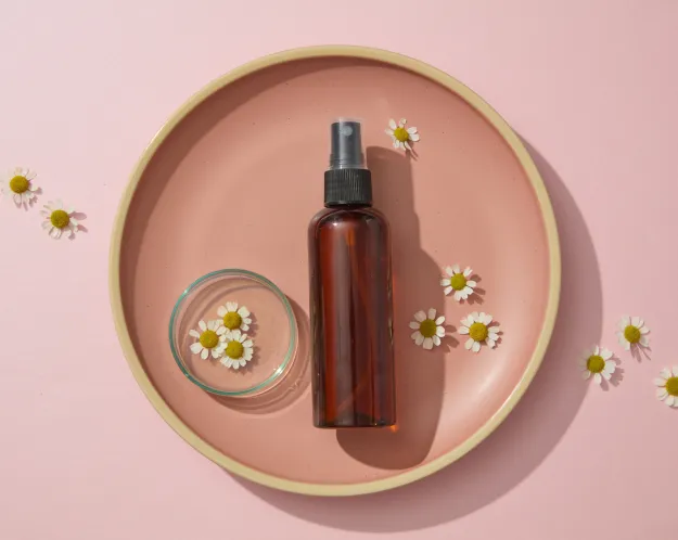 A brown spray bottle and chamomile flowers arranged on a pink plate, illustrating natural remedies for gum health.