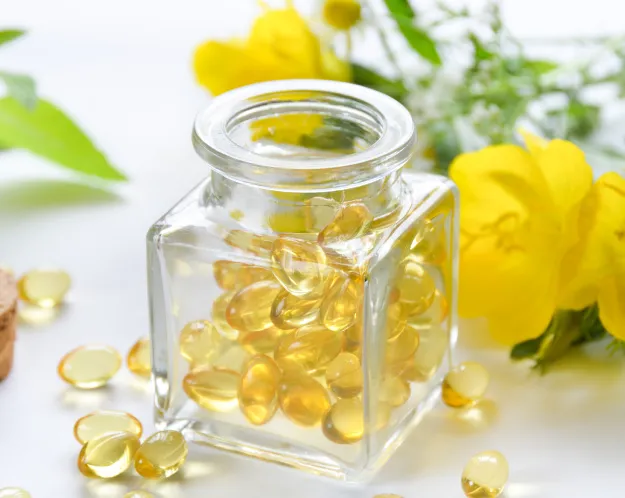 A glass jar filled with herbal supplement capsules, surrounded by fresh yellow flowers and greenery, emphasizing natural health remedies.