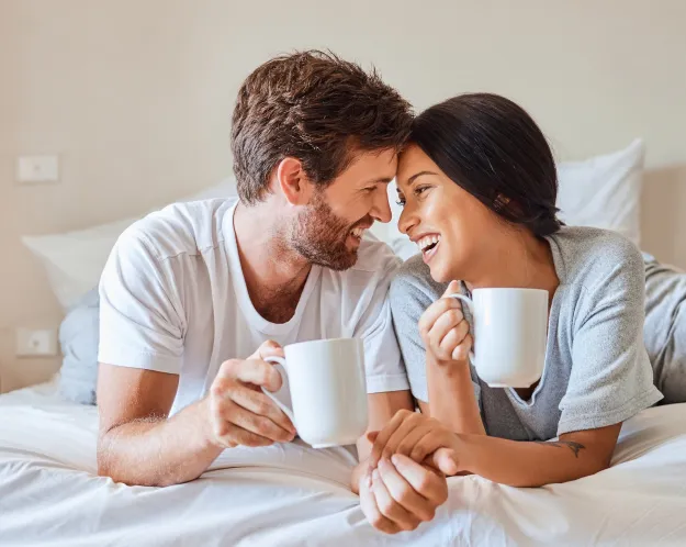 A happy couple enjoying a cozy moment together, holding mugs and smiling, symbolizing intimacy and connection.