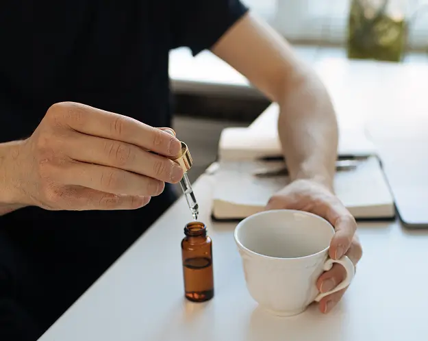 A man adding tincture drops into a cup of hot tea.